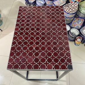 May include: A square table with a dark red tiled top featuring a white geometric pattern. The table has a black metal frame.