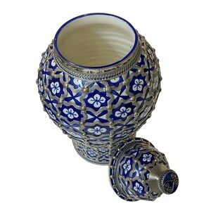 Puede incluir: Un tarro de cer&aacute;mica azul y blanco con una tapa de plata. El tarro tiene un patr&oacute;n geom&eacute;trico con motivos florales. La tapa tiene un pomo de plata.