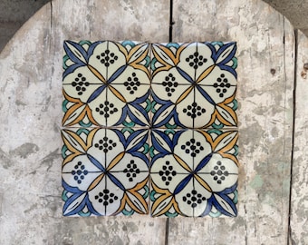 May include: Four square ceramic tiles with a floral design. The tiles feature a white background with a pattern of blue, yellow, orange, and green floral elements. Each flower has a cluster of black dots in the center.
