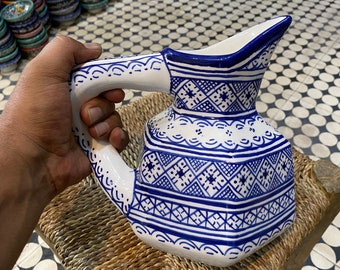 May include: A white ceramic pitcher with a blue and white geometric pattern. The pitcher has a wide spout and a handle.