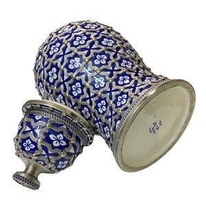 Puede incluir: Un tarro de cer&aacute;mica azul y blanco con detalles plateados y un patr&oacute;n geom&eacute;trico. El tarro tiene una tapa con un dise&ntilde;o similar. La parte inferior del tarro tiene una etiqueta con el texto "ع 12"