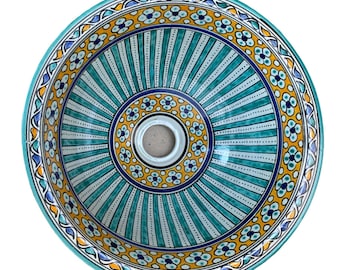 May include: Round ceramic sink with a hand-painted design. The sink features a central drain and a decorative pattern of teal, yellow, and blue floral and striped elements. The rim has a detailed border with floral motifs. The sink is a decorative bathroom fixture.