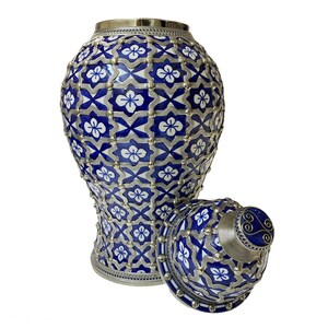 Puede incluir: Un jarr&oacute;n de cer&aacute;mica azul y blanco con una tapa plateada. El jarr&oacute;n tiene un patr&oacute;n geom&eacute;trico con detalles plateados. La tapa tiene un pomo plateado con un dise&ntilde;o de espiral.