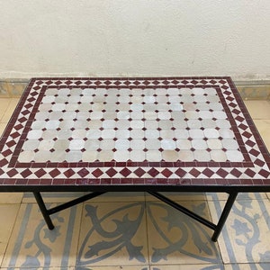 May include: A square coffee table with a white and burgundy mosaic tile top and a black metal frame.