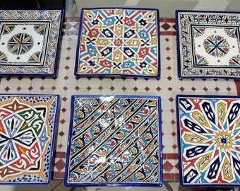 Może przedstawiać: Sześć kwadratowych ceramicznych talerzy z misternymi geometrycznymi wzorami w kolorze niebieskim, czerwonym, żółtym, zielonym i białym. Talerze mają niebieską obwódkę i są ułożone w dwóch rzędach po trzy.