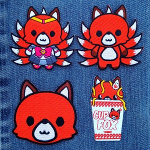 May include: Four embroidered patches featuring cartoon foxes. One fox is in a Sailor Moon-inspired outfit. Another fox has multiple tails. A third patch shows a fox face. The last patch shows a fox in a cup with the text "CUP FOX".