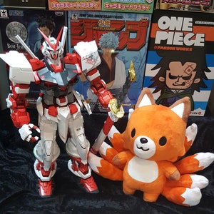 May include: A red, white, and gray robot toy stands on a black surface. A plush orange fox toy with nine tails sits in front of the robot. The fox toy has a white face and black eyes.