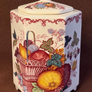 Peut inclure: Un pot en céramique hexagonal avec couvercle assorti, orné d'un motif de transfert coloré représentant un panier de fruits, des baies et des feuilles. La base blanc cassé est décorée d'illustrations rouges, jaunes, bleues et vertes.