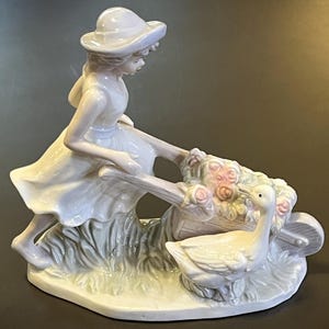 Porcelanowa figurka przedstawiająca dziewczynę pchającą wózek z kwiatami i gęsią.