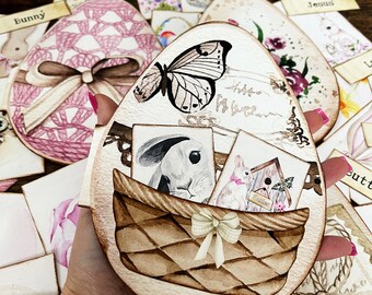 May include: A wooden Easter egg shaped ornament with a brown wicker basket, a white butterfly, and a white bunny rabbit. The basket has a white ribbon with a bow. The ornament has a distressed white background with the words "Hope Always" written in black.