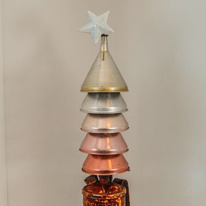 May include: A unique Christmas tree sculpture made from repurposed metal funnels and a vintage torch base. The tree is topped with a glittery star. The funnels are various shades of silver and copper, and the torch is rusty orange.