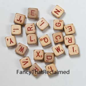 May include: A collection of wooden Scrabble tiles with red letters and numbers. The tiles are scattered on a white surface, with the text "Fancy That Reclaimed" visible in the lower left corner.