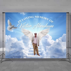 May include: A memorial backdrop with a blue sky and white clouds. The text "IN LOVING MEMORY OF Victor Abraham" is printed on the backdrop. A white dove and a pair of white angel wings are also depicted.
