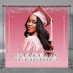 May include: Pink graduation backdrop with silver glitter and the text "Congratulations! KAMARIA CLASS OF 2024". A young woman in a pink graduation cap and gown is pictured in the background.
