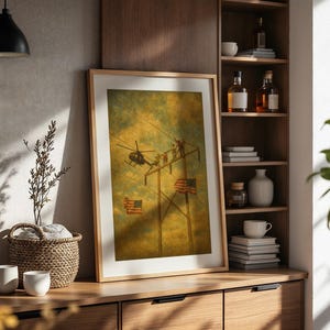 May include: A framed print featuring a vintage-style illustration of a helicopter and workers on a power line, with American flags. The artwork has a warm, sepia-toned color palette, and is displayed on a wooden cabinet.