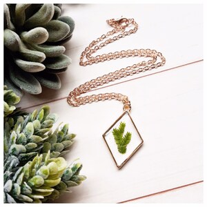 May include: A gold chain necklace with a diamond-shaped pendant featuring a pressed green leaf inside.