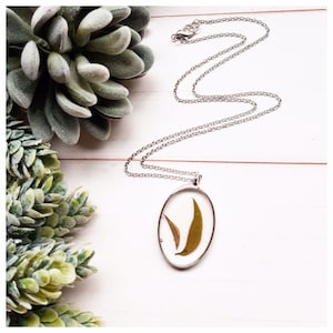 May include: A silver chain necklace with an oval pendant featuring two pressed green leaves encased in clear resin.