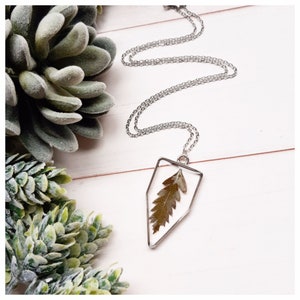 May include: A silver chain necklace with a geometric pendant featuring a pressed green leaf encased in clear resin.