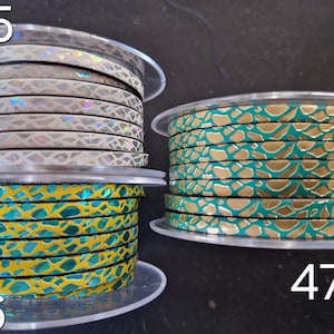 May include: Three spools of flat leather cord featuring textured patterns. Spool 45 has a white base with iridescent scales. Spool 46 is yellow with teal scale-like shapes. Spool 47 is teal with gold-colored metallic scale-like shapes.