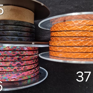 May include: Three spools of flat leather cord labeled 35, 36, and 37. Spool 35 features dark brown textured cord. Spool 36 displays a pink iridescent snakeskin pattern. Spool 37 contains bright orange cord with a raised, repeating geometric scale texture.
