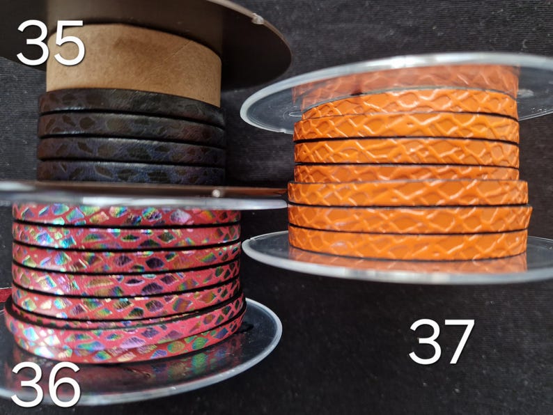 May include: Three spools of flat leather cord labeled 35, 36, and 37. Spool 35 features dark brown textured cord. Spool 36 displays a pink iridescent snakeskin pattern. Spool 37 contains bright orange cord with a raised, repeating geometric scale texture.