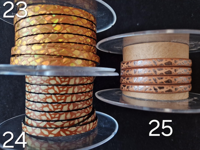 May include: Three spools of leather cord labeled 23, 24, and 25. Spool 23 features a metallic gold iridescent snakeskin pattern. Spool 24 displays a tan and white speckled design. Spool 25 shows a light brown cord with a dark brown textured pattern.