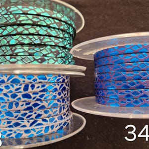 May include: Three spools of flat leather cord labeled 32, 33, and 34. Spool 32 features a black and metallic teal snakeskin pattern. Spool 33 displays a bright blue and silver mosaic design. Spool 34 shows a deep purple and blue snakeskin texture.