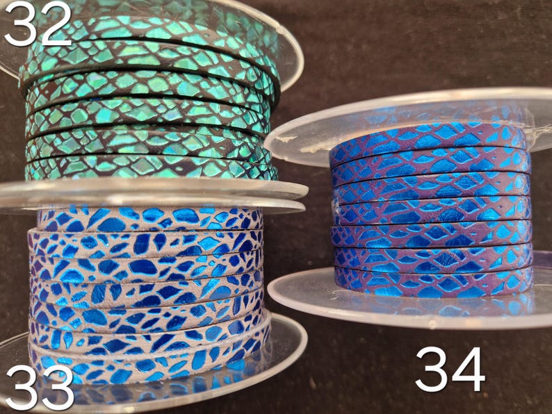 May include: Three spools of flat leather cord labeled 32, 33, and 34. Spool 32 features a black and metallic teal snakeskin pattern. Spool 33 displays a bright blue and silver mosaic design. Spool 34 shows a deep purple and blue snakeskin texture.