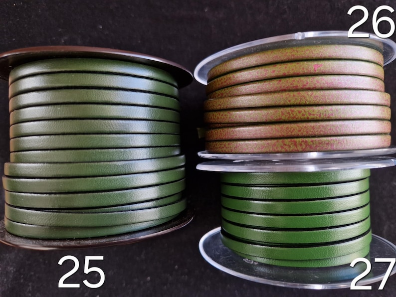 May include: Three spools of leather cord in shades of green and brown. The spools are labelled with the numbers 25, 26, and 27. The cord appears to be flat and is wound neatly around the spools, ready for crafting projects.