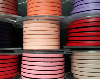 May include: Multiple spools of flat leather cord in various colors including red, orange, purple, dark blue, pink, and beige. Each spool features a clear plastic disc at the top and bottom, holding the stacked leather strips in place.