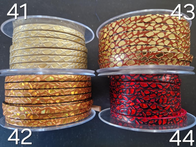 May include: Four spools of flat leather cord labeled 41, 42, 43, and 44. Spool 41 is metallic gold, 42 is iridescent bronze, 43 is metallic gold with a red crackle pattern, and 44 is black with a vibrant red crackle texture finish.