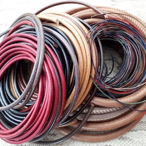 Peut inclure: Un tas de cordon en cuir de différentes couleurs, dont le rouge, le brun, le noir et le beige. Les cordons sont disposés en cercle, le cordon rouge étant le plus visible.