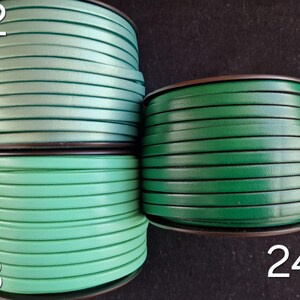 May include: Four spools of green leather cord. The spools are labelled with the numbers 22, 23, and 24. The cord is flat and tightly wound. The background is a dark colour. The cord is suitable for crafts.