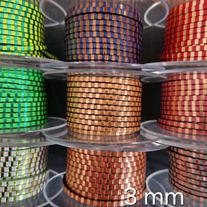 May include: Spools of decorative ribbon in various colors, including green, blue, red, and copper. The ribbon is 3 mm wide and has a checkered pattern. The spools are arranged on clear plastic holders.
