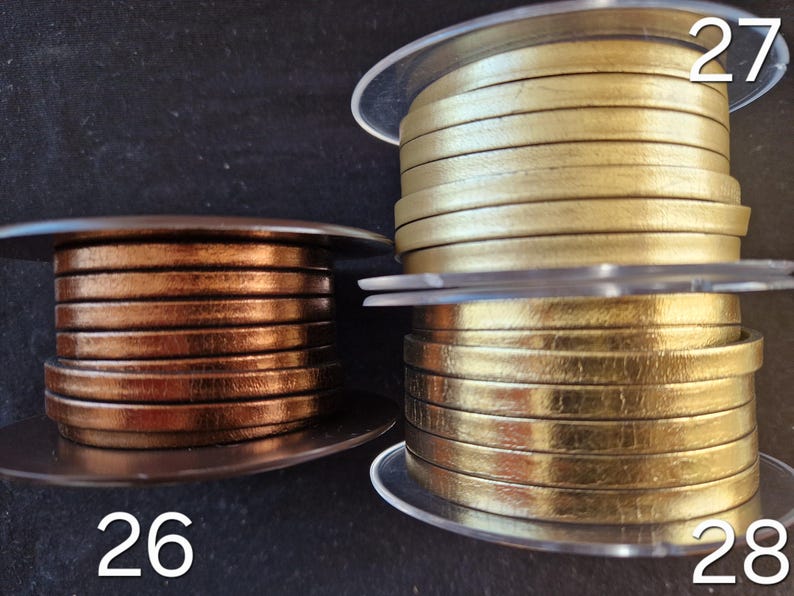 Pu&ograve; includere: Tre bobine di cordino in pelle piatta etichettate 26, 27 e 28. La bobina 26 &egrave; di colore bronzo metallizzato. La bobina 27 &egrave; di colore oro opaco. La bobina 28 &egrave; di colore oro lucido e riflettente. Ogni bobina &egrave; avvolta con pi&ugrave; strati di cordino.