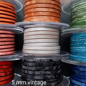 Peut inclure: Plusieurs bobines de cordon en cuir vintage de 5 mm, dans des couleurs variées : orange, rouge, argent, noir, vert et bleu. Le cordon est enroulé sur des bobines en plastique transparent. Le texte "5 mm vintage" est visible.
