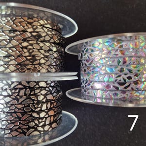 May include: Three spools of flat cord labeled 5, 6, and 7. Spool 5 features a black cord with a metallic gold mosaic pattern. Spool 6 displays a black cord with a metallic silver mosaic pattern. Spool 7 shows a white cord with an iridescent mosaic pattern.