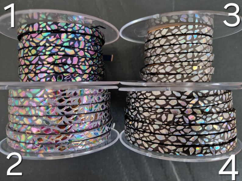 May include: Four spools of flat leather cord labeled 1 through 4. Spool 1 is black with iridescent shards. Spool 2 is light gray with iridescent shards. Spool 3 is light gray with silver shards. Spool 4 is black with silver and iridescent shards.