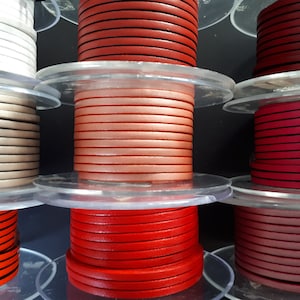 Pu&ograve; includere: Bobine di cordoncino in pelle colorato in varie tonalit&agrave;, tra cui bianco, beige, arancione, rosso e rosa. I cordoncini sono ordinatamente avvolti su bobine di plastica trasparente, ideali per l'artigianato e la creazione di gioielli.