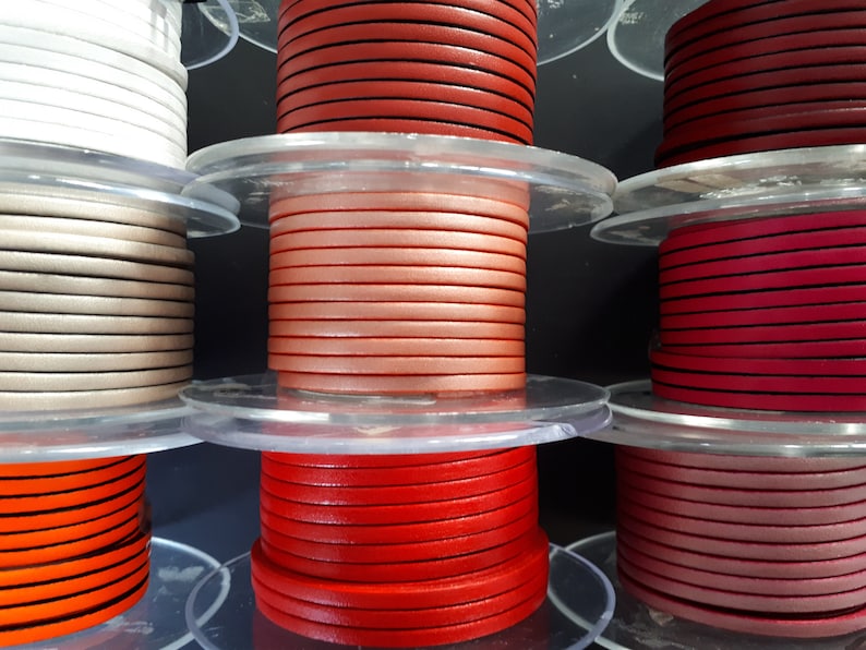 Pu&ograve; includere: Bobine di cordoncino in pelle colorato in varie tonalit&agrave;, tra cui bianco, beige, arancione, rosso e rosa. I cordoncini sono ordinatamente avvolti su bobine di plastica trasparente, ideali per l'artigianato e la creazione di gioielli.