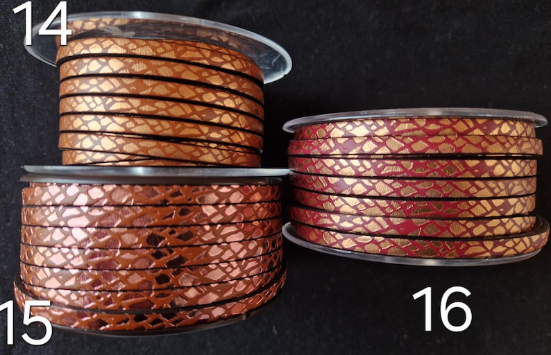 May include: Three spools of flat leather cord labeled 14, 15, and 16. Spool 14 is a metallic copper with a black snakeskin pattern. Spool 15 is a dark bronze with a black snakeskin pattern. Spool 16 is a metallic red with a gold snakeskin pattern.