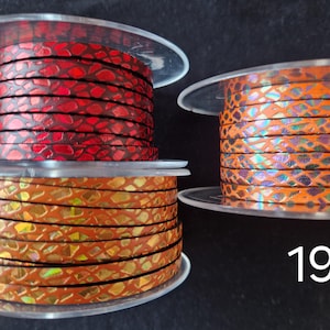 May include: Three clear plastic spools of flat leather cord labeled 17, 18, and 19. Spool 17 features a red snakeskin pattern, spool 18 has a metallic gold and orange scale design, and spool 19 displays an orange cord with iridescent scales.