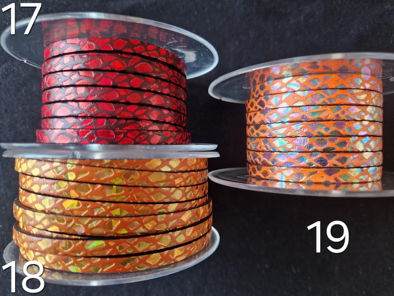 May include: Three clear plastic spools of flat leather cord labeled 17, 18, and 19. Spool 17 features a red snakeskin pattern, spool 18 has a metallic gold and orange scale design, and spool 19 displays an orange cord with iridescent scales.
