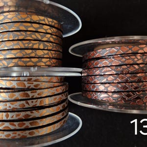 May include: Three spools of flat leather cord labeled 11, 12, and 13. Spool 11 features a metallic copper pattern on a dark base. Spool 12 displays a metallic copper pattern on a light gray base. Spool 13 shows a dark metallic copper scale pattern.