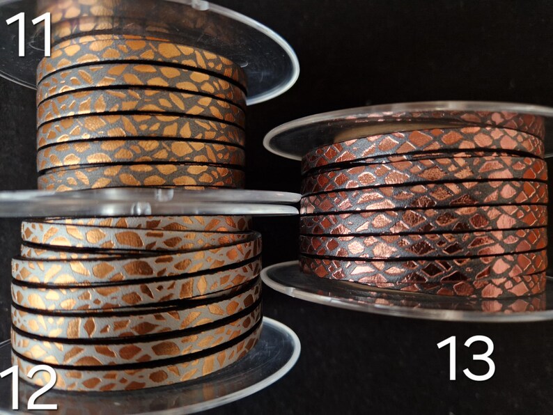 May include: Three spools of flat leather cord labeled 11, 12, and 13. Spool 11 features a metallic copper pattern on a dark base. Spool 12 displays a metallic copper pattern on a light gray base. Spool 13 shows a dark metallic copper scale pattern.