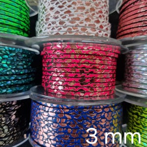 Può includere: Diverse bobine di cordino in pelle piatta da 3 mm di larghezza con un motivo metallico simile alla pelle di serpente in vari colori, tra cui verde brillante, rosa acceso, blu reale, argento e nero, avvolte su bobine di plastica trasparente.