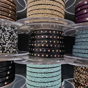 Peut inclure: Bobines de différents galons et embellissements, dont du cuir noir avec des clous argentés, des paillettes noires et blanches, des perles turquoise et du cuir marron avec des clous dorés.