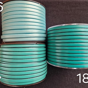 May include: Three spools of teal and turquoise leather cord. The flat cord is approximately 3mm wide. The spools are labelled with the numbers 16, 17, and 18. The cord is wound neatly on the spools.