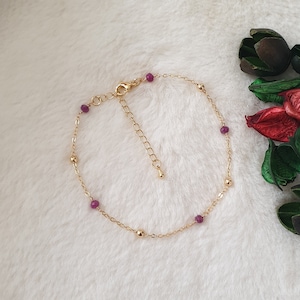 Puede incluir: Un delicado brazalete de cadena dorada con pequeñas cuentas moradas. El brazalete tiene un cierre de mosquetón y una cadena extensora.