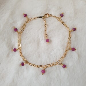 Peut inclure: Un bracelet de cheville en chaîne dorée avec une double rangée de chaîne et des pierres précieuses roses pendantes.